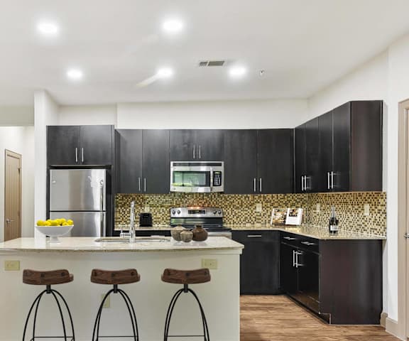 a kitchen with black cabinets and a counter top with three stools at Lakeline East Apartments, Cedar Park, TX