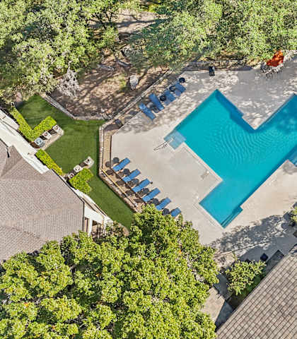 An aerial view of a swimming pool surrounded by trees and a few lounge chairs at TalaVera Apartments, San Antonio, Texas