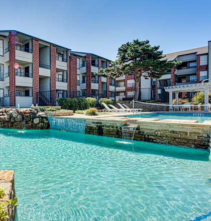A swimming pool surrounded by a stone wall and a variety of plants.
