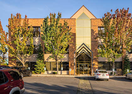 A building with a glass facade is surrounded by trees and cars.