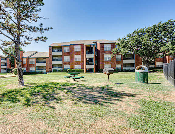 A tree stands in a grassy area in front of apartment buildings.