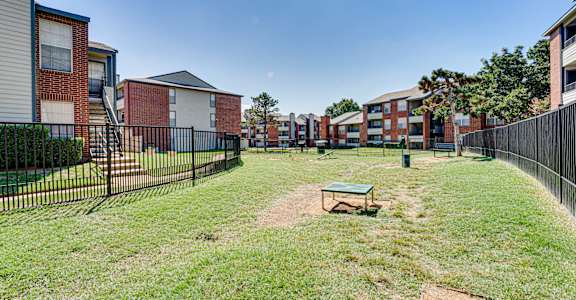 A grassy area with a bench and a baseball diamond in front of apartment buildings.