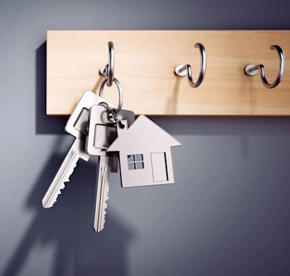 A set of keys is hanging from a hook on a wooden board with the word "home" written on it.