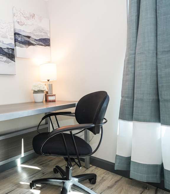 A bedroom with a bed, desk, chair, and a painting on the wall.