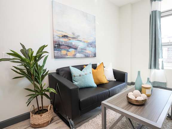 A living room with a black couch, a wooden coffee table, and a large painting on the wall.