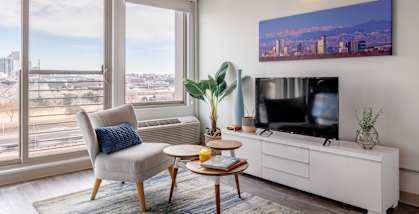 A living room with a chair, a table, a television, and a large window overlooking a cityscape.