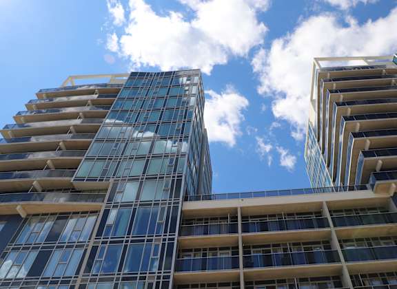 Two modern glass buildings with balconies in front of a blue sky with clouds.