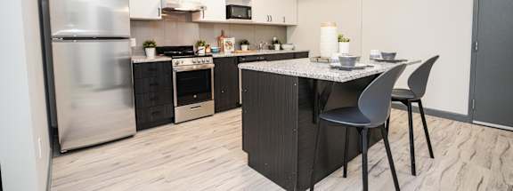 A modern kitchen with a stainless steel refrigerator and a marble top island.