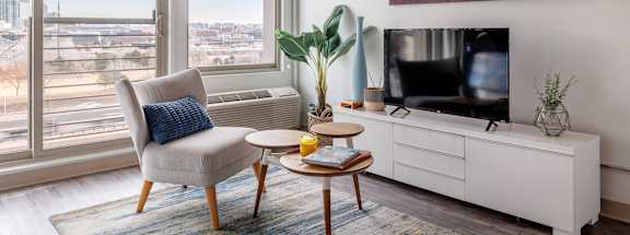 A living room with a chair, a table, a television, and a large window overlooking a cityscape.