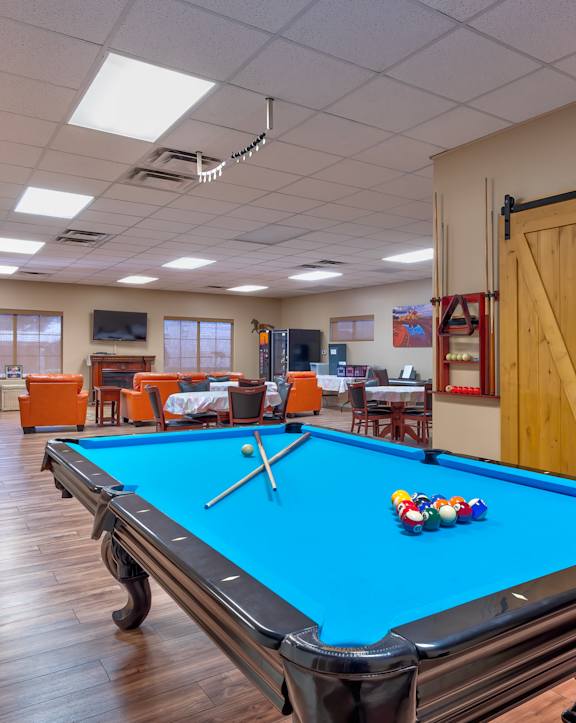 a pool table in the clubhouse of a community center with a gym and exercise equipment