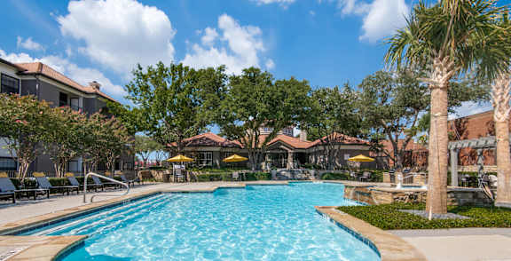 A large swimming pool surrounded by palm trees and lounge chairs.