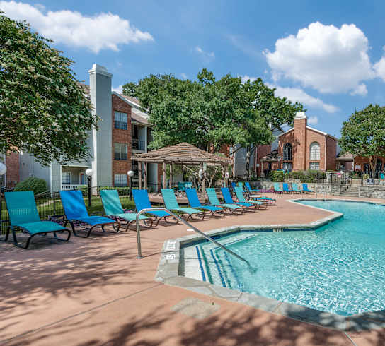 a resort style swimming pool with blue chairs and a building in the background at Foxborough Apartments, Irving, TX