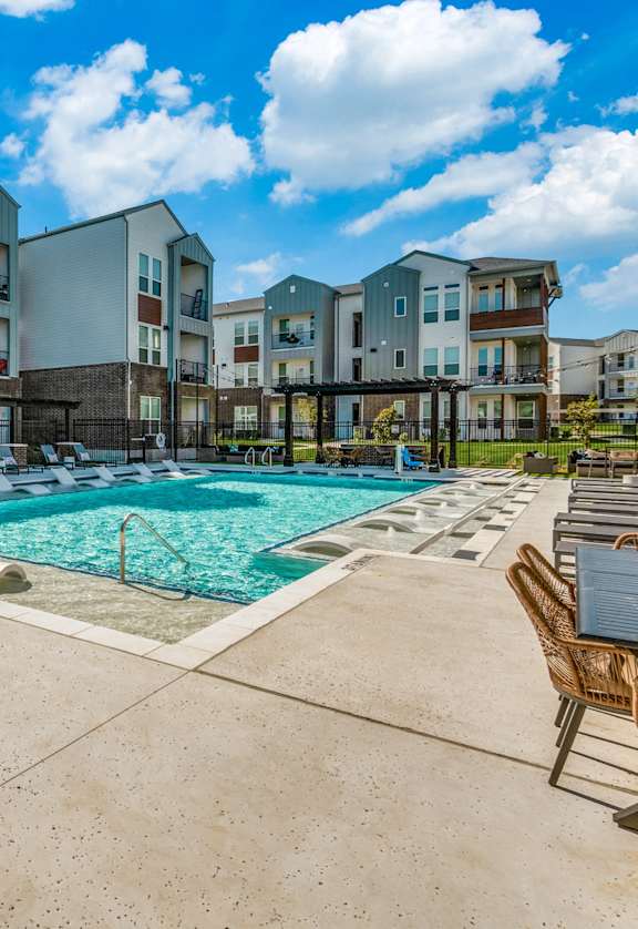 A large swimming pool surrounded by chairs and buildings.