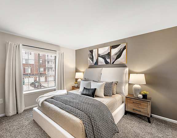 A bedroom with a large bed and a window with white curtains.