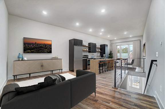 a living room with a couch and a chair and a kitchen with a staircase