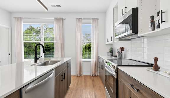 A modern kitchen with white countertops and wooden floors.