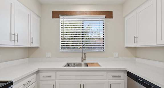 A kitchen with white cabinets and a window with blinds at San Xavier Casitas, Tucson