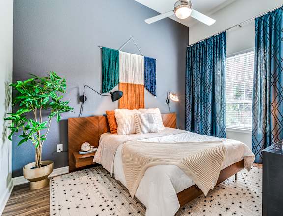 A bedroom with a bed, a potted plant, and a ceiling fan.