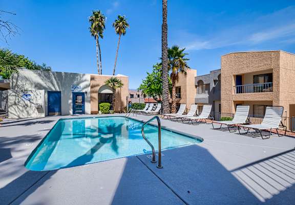 our resort style swimming pool is next to a building and palm trees