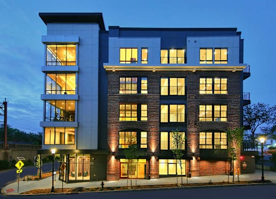 An apartment building with a mix of brick and panel construction is illuminated at dusk.