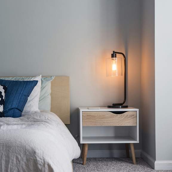 A bed with a white comforter and a lamp on a side table.