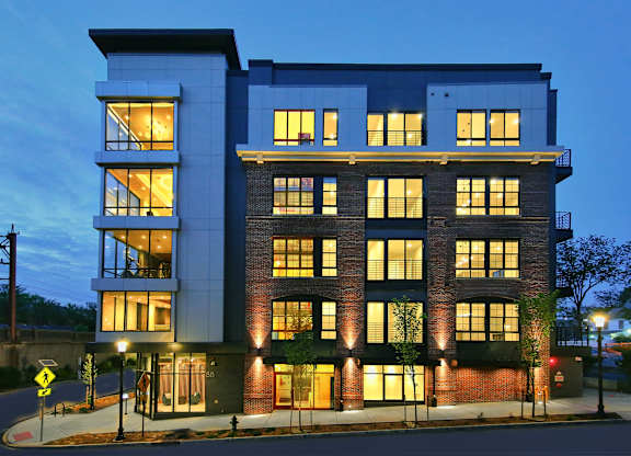 An apartment building with a mix of brick and panel construction is illuminated at dusk.