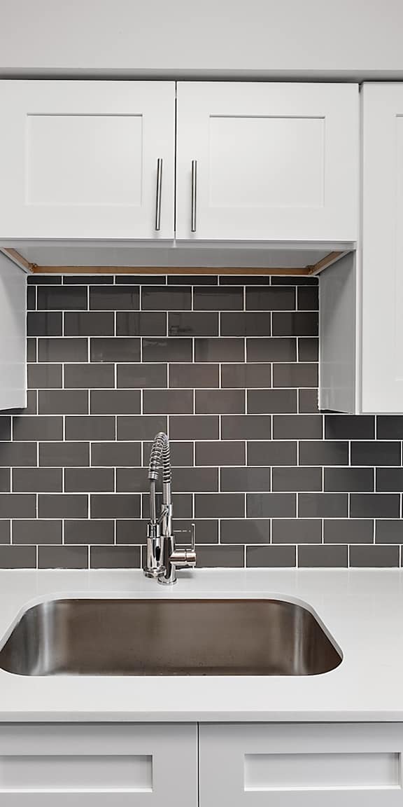 A kitchen with white cabinets and a black tile backsplash.