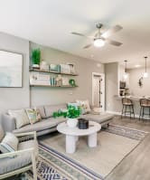 a living room with a couch, chair, and coffee table with plants and a kitchen in the background at vantage apartments