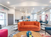 Thumbnail 4 of 11 - A brightly lit room with a large orange couch and a coffee table in the center.