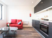 Thumbnail 4 of 8 - a living room with a red couch and a table with a vase of flowers