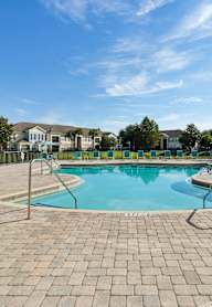 A swimming pool surrounded by a brick patio and lounge chairs.
