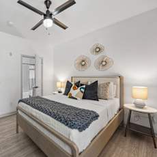 A bedroom with a bed, a ceiling fan, and a side table.
