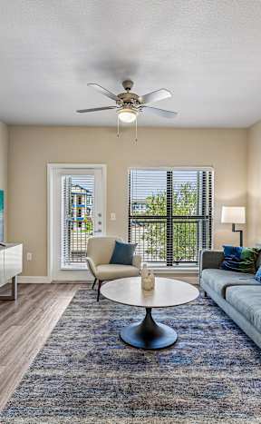 A living room with a grey couch, a round table, and a ceiling fan.