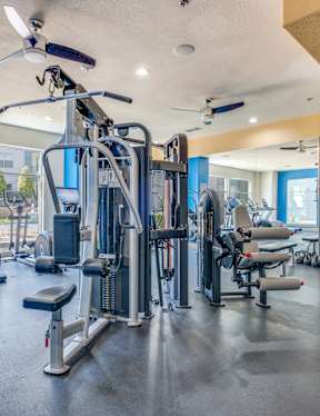A spacious gym with a variety of equipment including treadmills, weight machines, and a ceiling fan.