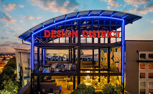 A modern building with a glass facade and a blue neon sign that reads "Design District".