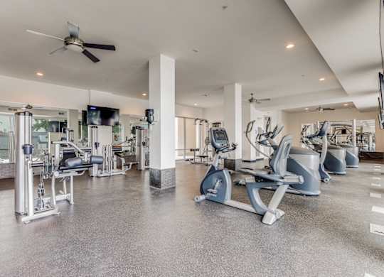 a gym with cardio machines and a ceiling fan