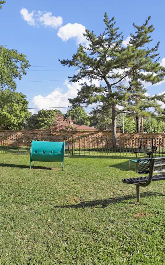 A park with a bench, trees, and a fence.