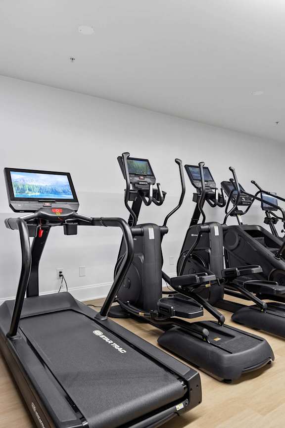 A spacious room with a mirror, exercise equipment, and a television displaying a sunset.
