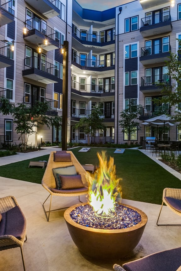 an outdoor lounge area with a fire pit in front of an apartment building