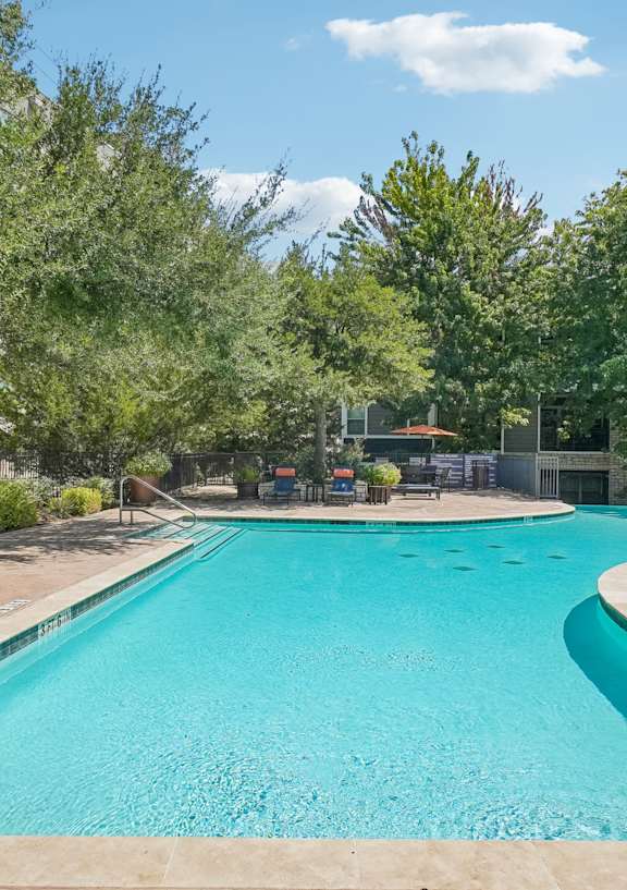 A large outdoor swimming pool surrounded by trees and a fence.