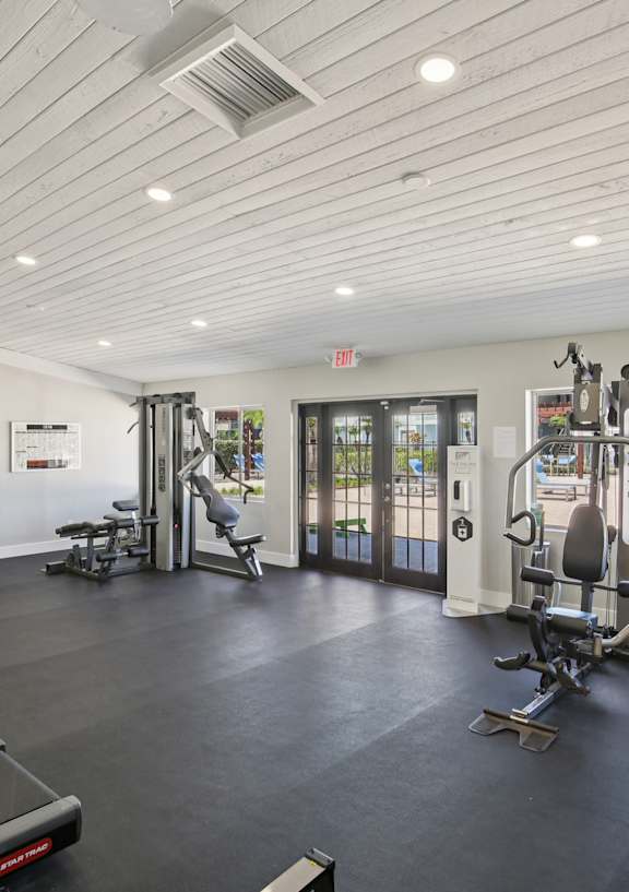 A spacious gym with a variety of equipment and a view of the pool outside.