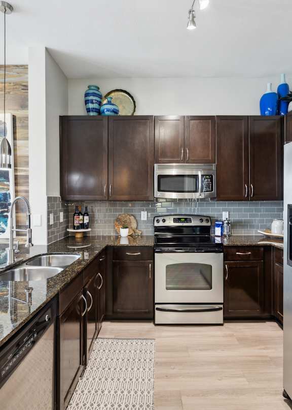 A modern kitchen with a stainless steel refrigerator, black countertops, and wooden cabinets.