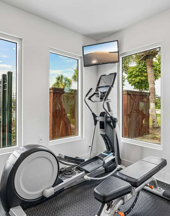 A home gym with a stationary bike and a view of the backyard through the windows.