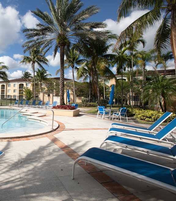 A playground with a slide and swings in front of a building with palm trees.
