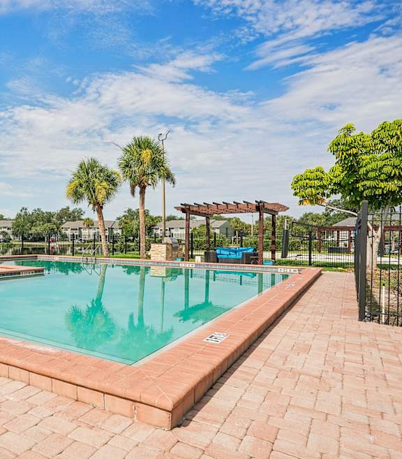 A pool surrounded by a brick patio with a palm tree in the background.