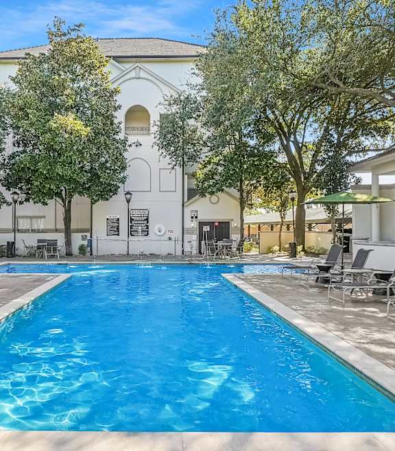A large swimming pool surrounded by lounge chairs and trees.