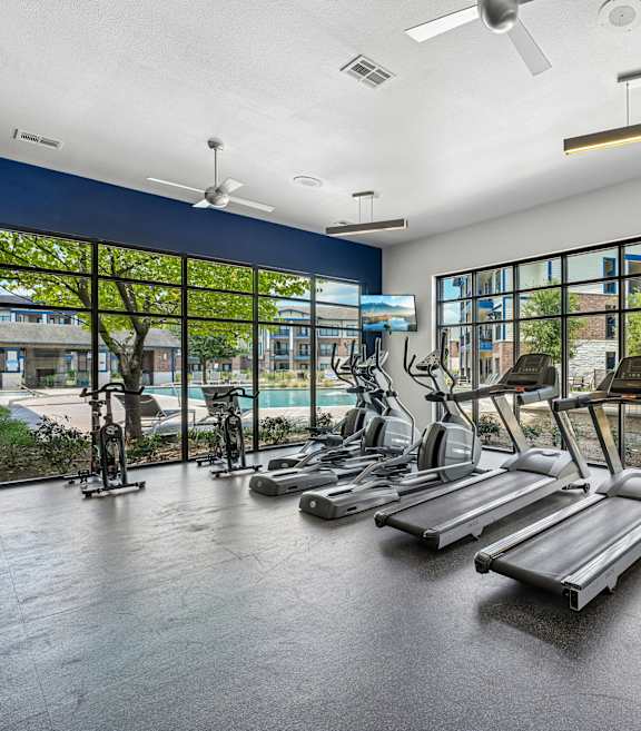 A gym with a row of treadmills and exercise bikes.