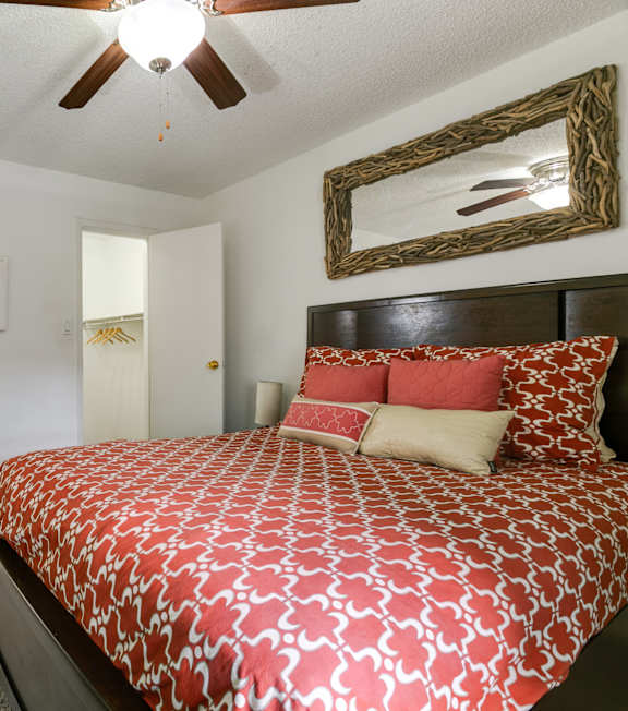 A bedroom with a patterned bedspread and a ceiling fan.