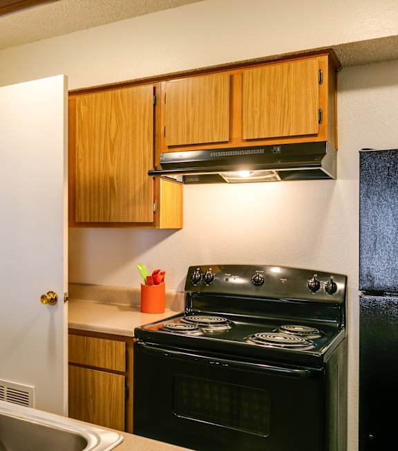 A kitchen with a black stove and wooden cabinets.