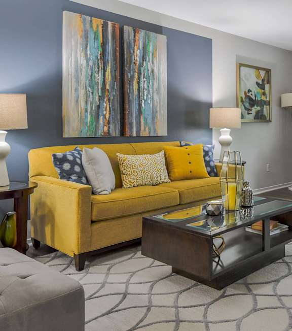 A living room with a yellow couch and a grey ottoman.